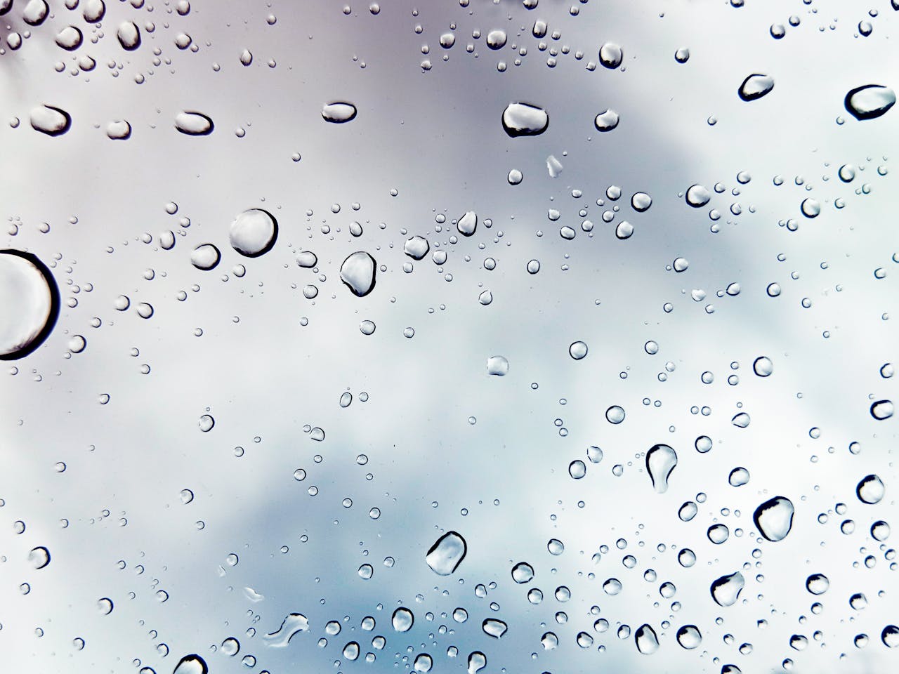 Raindrops on a window against a cloudy sky, creating a peaceful mood.